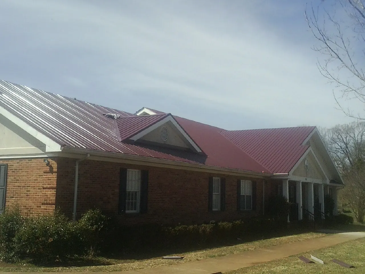 Red metal roof with gabled entries on a long brick building, from a Hail Damage Roof Repair job in Caseyville