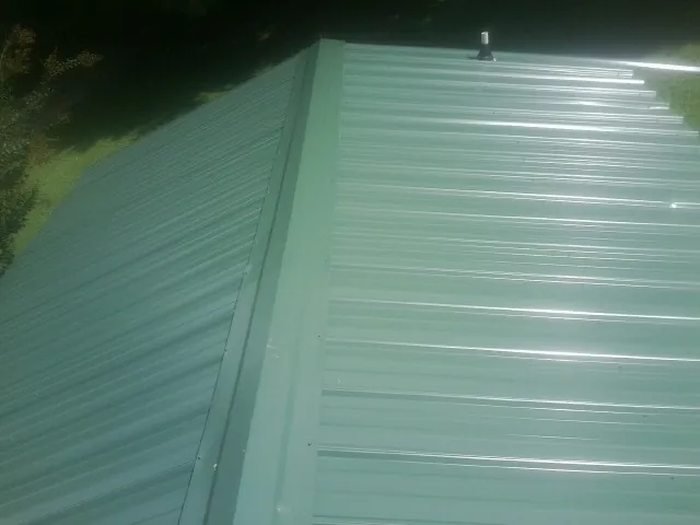 New green metal panels meeting at the ridge of a roof — Flat Roof Repair work by our crew in Caseyville
