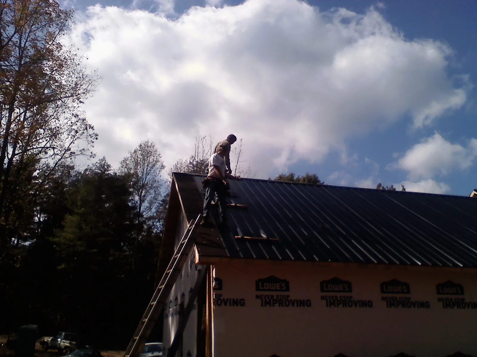 Roofer fastening dark metal panels high against a cloudy sky, from a Roof Inspection job in Caseyville